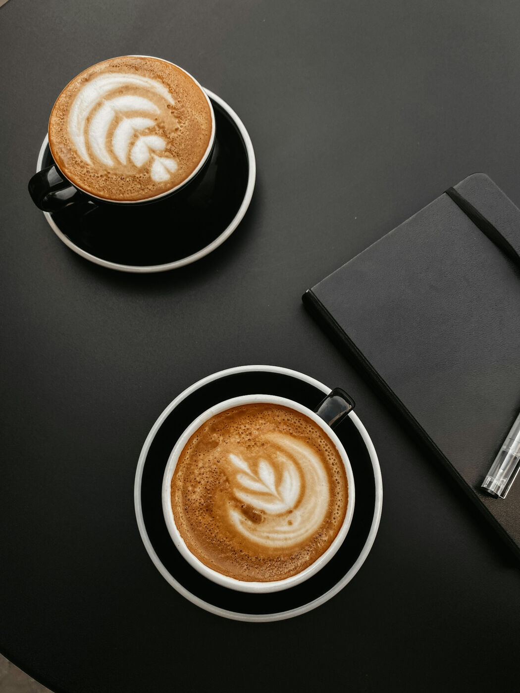 Two cappuccinos and a notebook on a dark table